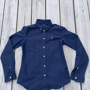 Ralph Lauren skjorta - Säljer en klassisk Ralph Lauren-skjorta i marinblått. Skjortan har button-down krage och den ikoniska loggan på bröstet. Storlek xs och i mycket fint skick. Passar lika bra till vardags som till mer uppklädda tillfällen. Om du har några funderingar eller vill ha fler bilder är det bara att skriva!🙌 Pris kan diskuteras.