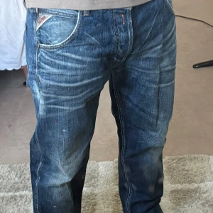 Replay Geebo jeans blå wide fit - Säljer ett par Replay Geebo jeans i blå tvätt med coola slitningar och kontrastsömmar. Modellen har bred passform och klassiska fem fickor, med Replay-logga på fickan. Tillverkade i Italien av slitstarkt jeanstyg. Perfekt för dig som gillar avslappnad stil. Köpta för 1500kr.
