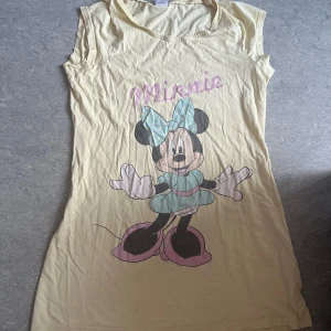 Gul Disney klänning med Minnie Mouse - Kan användas som en söt nattlinne. Passformen är stor. Säljet en gul kortklänning från Disney med stort tryck av Minnie Mouse på framsidan. Klänningen har ärmlös design och rund hals. Trycket har detaljer i ljusblått, rosa och svart. Perfekt för dig som älskar Disney och vill ha en lekfull stil.