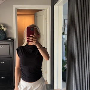 Svart croppad polotopp - Snygg svart polotopp med croppad passform och ärmlös design. Perfekt att styla med höga jeans eller kjol för en cool look. Tunn och mjuk kvalitet som sitter tight mot kroppen och ger en clean siluett.