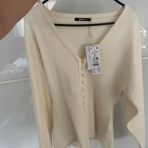 Krämvit stickad kofta från Gina  - Säljer en krämvit stickad kofta från Gina Tricot med v-ringning och knappar framtill. Koftan har lång ärm och är mjuk i materialet, perfekt för lager-på-lager. Enkel och stilren design som passar till mycket.