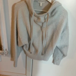 Vit croppad hoodie från H&M - Mysig vit hoodie från H&M i croppad modell. Tröjan är stickad med långa ärmar, huva och dragsko. Perfekt för en avslappnad och trendig look.