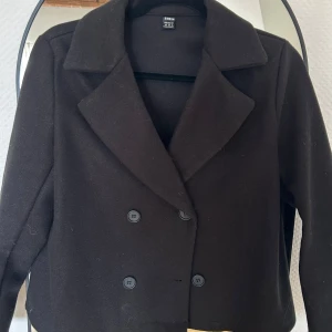 Svart kavajjacka från SHEIN - Stilren svart kavajjacka från SHEIN med dubbelknäppning och breda slag. Jackan har en klassisk, rak passform och är tillverkad i ett mjukt material som känns lyxigt. Perfekt för dig som vill ha en snygg och enkel look.