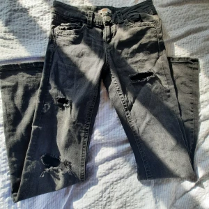 Svarta slitna jeans med trasiga detaljer - Säljer ett par svarta jeans med snygga trasiga detaljer på benen. Jeansen har fem fickor, knappgylf och coola bakfickor med lock och knapp. Perfekta för en avslappnad streetstil. Materialet är klassisk denim. SÄLJER FLER JEANS!!!!❤️❤️❤️❤️