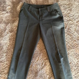 Mörkgrå kostymbyxor  - Snygga mörkgrå kostymbyxor från Buonq med raka ben och låg midja. Byxorna har knappar i midjan och bakficka med knappdetalj. Perfekta för en stilren look.