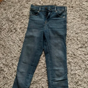 Blå skinny jeans - Säljer ett par klassiska blå skinny jeans med normalhög midja. Jeansen har fem fickor, dragkedja och knapp framtill. Perfekta till vardags och lätta att matcha med olika toppar.