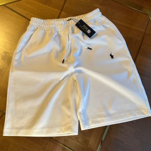Vita shorts från Polo Ralph Lauren - Snygga vita shorts från Polo Ralph Lauren med elastisk midja och snörning. Klassisk logga broderad på vänster ben. Perfekta för en avslappnad stil och har två sidofickor.