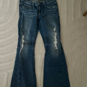 Blå bootcut jeans med slitningar - Säljer ett par blå bootcut jeans med slitna detaljer framtill. Dom är från gina 14+ i storlek M