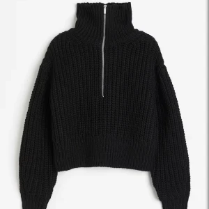 Svart stickad tröja med dragkedja från H&M - Säljer en svart, grovstickad tröja från H&M med hög krage och dragkedja framtill. Tröjan har lång ärm och en oversized passform, perfekt för kyliga dagar.
