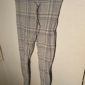 Grå-rutiga pyjamasbyxor - Säljer ett par gråa pyjamasbyxor med blå och vita rutor. Byxorna har snörning i midjan och är raka i modellen. Perfekta för en avslappnad stil och tillverkade i ett lätt bomullsmaterial.💓