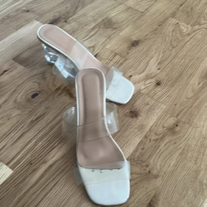 Vita klackskor med transparent rem - Säljer ett par trendiga vita klackskor med transparenta remmar och fyrkantig tå. Skorna har en genomskinlig klack som ger en modern look. Perfekta för dig som vill sticka ut med en stilren.