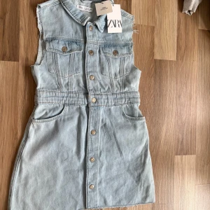 Ljusblå ärmlös jeansklänning från Zara - Superfin ljusblå jeansklänning från Zara med krage, knappar hela vägen fram och råa kanter vid ärmhålen. Klänningen har fickor både fram och bak och är i en kort modell. Perfekt för en cool och avslappnad look. säljer eftersom att den inte passar mig. pris går att diskuteras