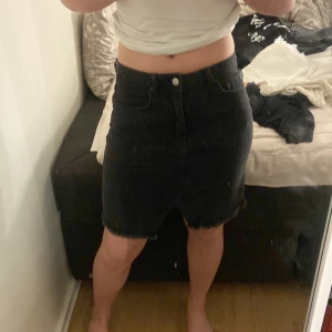 Svart jeanskjol från NA-KD, stl 38 - Svart jeanskjol från NA-KD i storlek 38. Kjolen är kort, har rå kant nertill och klassisk femficksdesign. Snygg, enkel och passar perfekt till sneakers eller boots. Hög midja och dragkedja framtill.