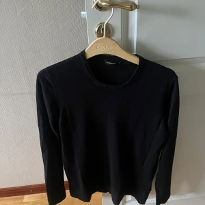 Svart långärmad tröja J.Lindeberg - En stilren svart långärmad tröja från J.Lindeberg. Tröjan har rund halsringning och är i ett mjukt, tunt material som passar perfekt till lager-på-lager. Enkel och clean design utan synliga detaljer eller mönster.