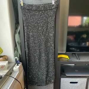 Glittrig långkjol från Weekday - Supersnygg långkjol från Weekday i svart med massor av glittrande paljetter. Kjolen har rak passform och resår i midjan för extra komfort. Perfekt för dig som vill sticka ut och glänsa lite extra.