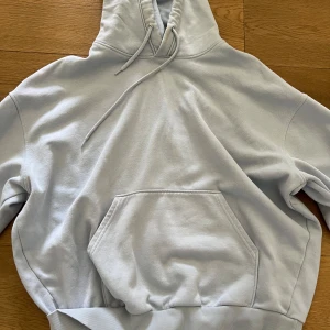 Ljusgrå hoodie från Weekday - Säljer en ljusgrå hoodie från Weekday med klassisk känguruficka och huva med dragsko. Tröjan har ribbade muddar och är perfekt för en avslappnad stil. Supermjuk insida och enkel att matcha med det mesta.