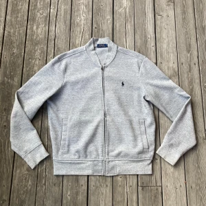 Grå ”bombertröja” från Polo Ralph Lauren - Härlig grå bombertröja från Ralph Lauren i mycket bra skick. Tröjan är i storlek L och passsr sin storlek. Perfekt som ett andra lager nu på sommaren! Hör av er om frågor!