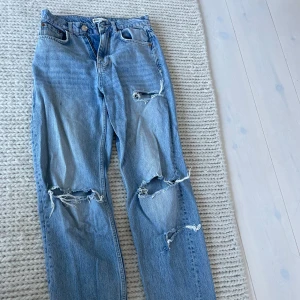 Ljusblå slitna jeans från g perfect jeans - Säljer ett par ljusblå jeans från g perfect jeans med flera slitningar och hål på både fram- och baksida. Jeansen har klassisk femficksdesign, raka ben och normal passform. Perfekta för en avslappnad och trendig look.