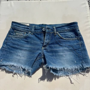 Blå jeansshorts med nitar - Snygga blå jeansshorts från Dondup, men köpte second hand. Fransig kant och coola nitar på fickorna. Klassisk femficksmodell med låg midja och slitna kanter. Aldrig använda. Skulle säga att de passar XS/S