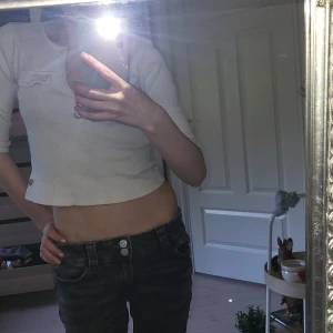 Vit croppad ribbad topp med dragkedja - Säljer en vit croppad topp med ribbad struktur och dragkedja framtill. Toppen har korta ärmar och en liten fickdetalj på bröstet. Perfekt för en trendig och avslappnad stil.