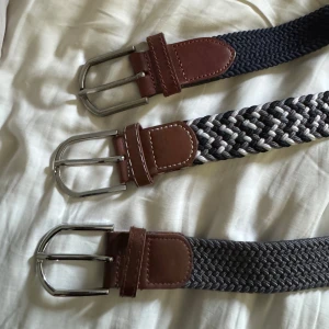 Tre flätade bälten med bruna skinn-detaljer - Säljer tre snygga flätade bälten med bruna skinn-detaljer och silverfärgade spännen. Ett bälte är helgrått, ett är svart och vitt, och ett är mörkblått. Perfekta accessoarer för att lyfta din outfit. Det blåa är 105 och dem andra är 95 cm! 50 kr styck