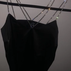 Svart satinlinne med glittriga band - Superfin top med glitter band som korsar i ryggen. Med ett slags silke tyg, där linnet  är inte använd där jag bara har tagit bort prislappen. 