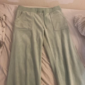Ljusgröna mjukisbyxor från Juicy Couture - Säljer ett par ljusgröna mjukisbyxor från Juicy Couture med bred resår i midjan och dragsko. Byxorna har stora fickor fram och en ficka med lock bak. Perfekta för en avslappnad stil, byxorna är av kortade vid benen, passar runt längden 150cm om man vill att byxorna ska vara lite långa,fast 155 om de ska vara perfekta.