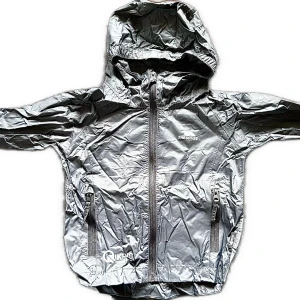 Grå vindjacka med huva från Trespass Ny - Säljer en grå vindjacka från Trespass, modell Qikpac. Jackan har huva, dragkedja framtill och två fickor med dragkedja. Den är lätt, vattentät och andas, perfekt att packa ner i medföljande påse. Barnjacka stl 98