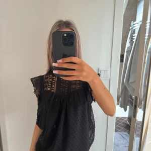 Svart blus med spets och volang - Säljer en svart blus med fina spetsdetaljer upptill och volanger vid axlarna. 