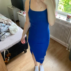 Blå tight klänning med slits - Säljer en blå tight klänning med smala axelband och slits på sidan. Klänningen är figurnära och har en enkel, stilren design som passar perfekt för sommardagar eller utekvällar. Materialet känns mjukt och stretchigt.
