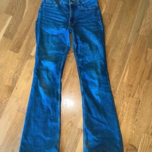 Blå bootcut jeans från H&M Divided - Säljer ett par lågmidjade blå bootcut jeans från H&M Divided i storlek 36. Jeansen har en klassisk femficksdesign. Perfekta för dig som gillar en retroinspirerad look med utsvängda ben. Lite slitna längst ner.