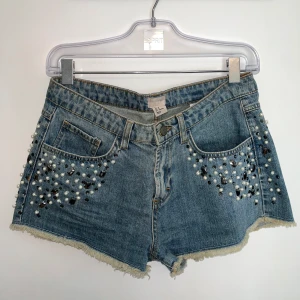 Jeansshorts med pärlor & stenar  - Snygga blå jeansshorts från H&M dekorerade med pärlor och stenar i olika former framtill. Klassisk femficksmodell och hög midja. Perfekta för sommaren! 💙