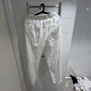 Vita linnebyxor med resår och snörning - Säljer ett par vita linnebyxor med resår i midjan och snörning framtill. Byxorna har en avslappnad passform och är perfekta för varma dagar. Lätta och luftiga med enkel design.