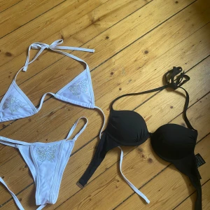 Två bikinis  svart & vit - Säljer två bikinis! En vit bikini med glittriga fjärilar i strass och smala knytband, samt en svart vadderad bikiniöverdel från H&M med bygel och knäppning bak. Perfekta för stranden eller poolen i sommar. Använda max 1 gång. 50kr för en eller 70 för båda