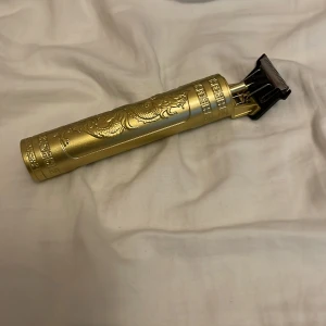 Guldig trimmer med drakmönster - Säljer en elektrisk trimmer med snyggt drakmönster ingraverat på handtaget. Färgen är guldig och designen är riktigt lyxig. Perfekt för att fixa detaljerade linjer och kanter. Medföljer flera svarta kammar i plast.