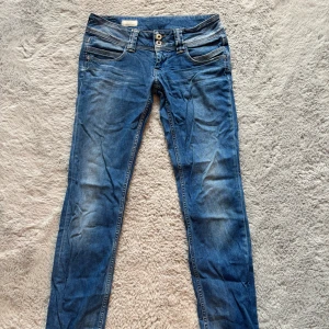 Blå jeans från Pepe Jeans - Snygga blå jeans från Pepe Jeans med coola slitningar och dubbla knappar i midjan. Klassiska femficksmodellen med broderade detaljer på bakfickorna och Pepe Jeans-logga. Dom är i storlek Waist 28 och inseam 34.💓