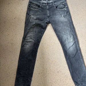 Replay anbass 05 aged  - Snygga svarta Replay jeans med slitningar och tvättad look. Modellen är slim fit med klassiska fem fickor och detaljerade bakfickor. Jeansen har dragkedjegylf och är tillverkade i stretchig bomullsdenim för en bekväm passform.