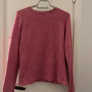 Rosa stickad tröja från vero moda - Mysig rosa stickad tröja med rund halsringning och långa ärmar. Tröjan har ribbade muddar vid hals, ärmslut och nederkant. Perfekt för att hålla sig varm under kyliga dagar.