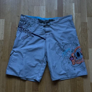 Billabong Gråa Board Shorts - Billabong board shorts i färgen grå. Storlek: 40, Midja: 50 cm Ytterben: 59 cm Benöppning: 34 cm Material: 100% Polyester.