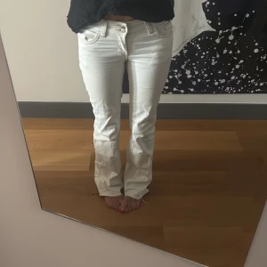 Vita bootcut jeans med broderi - Säljer ett par vita jeans med bootcut-modell och snygga broderade detaljer på bakfickorna. Byxorna har låg midja, klassiska fickor och markerade sömmar. Perfekta för dig som vill ha en clean och fräsch look med lite edge. Det är smått missfärgade nere vid hälen men inget som syns tydligt. 