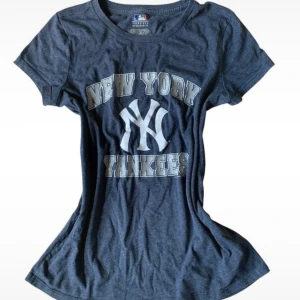 New York Yankees t-shirt MLB - Mörkblå t-shirt med New York Yankees-tryck framtill. Klassisk rund hals och korta ärmar. Tillverkad i mjuk bomullsblandning, perfekt för dig som vill visa ditt stöd för Yankees på ett stilrent sätt.