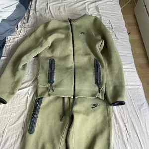 Grön Nike tech fleece  - Säljer en olivgrön hoodie från Nike med hel dragkedja och svarta detaljer. Tröjan har två fickor med dragkedja och en stilren Nike-logga på bröstet. Perfekt för dig som gillar sportig och clean stil.