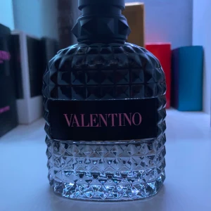 Valentino Born In Roma 100 ml - Valentino Uomo Born In Roma är en lyxig herrparfym i en cool, mörkgrå glasflaska med nitar och rutmönster. Flaskan har en svart etikett med rosa text och svart mattsvart kork. Doften är modern och elegant, perfekt för dig som gillar exklusiva parfymer. Typ helt full! 100 ml