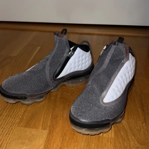 Nike Jordan Proto Max 720 grå/vit - Unika Nike Jordan Proto Max 720 sneakers i grått och vitt med futuristisk design. Ovandel i glittrig grå textil, vita paneler med prickstruktur och dragkedja på sidan. Sulan är genomskinlig med röd detalj undertill. Perfekta för dig som vill sticka ut.