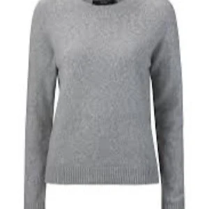 Grå stickad tröja med rund hals - En enkel och stilren grå stickad tröja med rund halsringning och långa ärmar. Tröjan har ribbade muddar vid ärmslut och nederkant, vilket ger en snygg och klassisk look. Perfekt att matcha med jeans eller kjol.