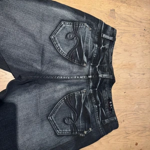 Svarta jeans från EDI med broderade fickor - Säljer ett par svarta jeans från EDI med snygga broderade bakfickor och coola slitningar. Jeansen är bootcut med loosefit och färgen är mörk med ljusare tvättade partier. Y2k stil 🫶🏻 