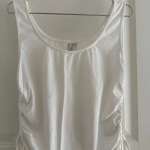 Vit linnetopp med snörning NLY Trend - Säljer en vit ärmlös linnetopp från NLY Trend i storlek L. Toppen har snygg snörning och rynkade detaljer på sidorna som ger en cool och trendig look. Mjuk och skön bomullskänsla, perfekt till jeans eller kjol.