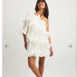 Vit oneshoulder volangklänning - Super fin vit kortklänning med volanger och plisserade detaljer. Klänningen har oneshoulder-design med en ärm och böljande volanger över hela plagget. Perfekt för dig som vill sticka ut och älskar statement-plagg!