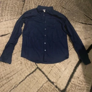 Mörkblå skjorta från D.M.D - Snygg mörkblå skjorta från D.M.D by denim day i storlek 158/164. Skjortan har klassisk krage, långa ärmar och knäppning med knappar framtill. Materialet är mjuk bomull som känns skönt mot huden. Perfekt för dig som gillar stilrena och enkla plagg.