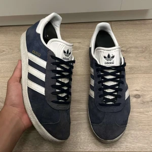 Adidas Gazelle skor - Snygga Adidas Gazelle skor i mörkblå mocka till salu | Knappt använda, köpta förra året men användes endast i 1 månad | Storlek: 41 1/3 | Skick: 7.5/10, inga defekter | Skorna passar fint till det mesta och är stilrena | Kvitto finns ifall man vill ha det | Nypris 1250kr, vårat är 699kr | Skriv gärna ifall du är intresserad 🙂